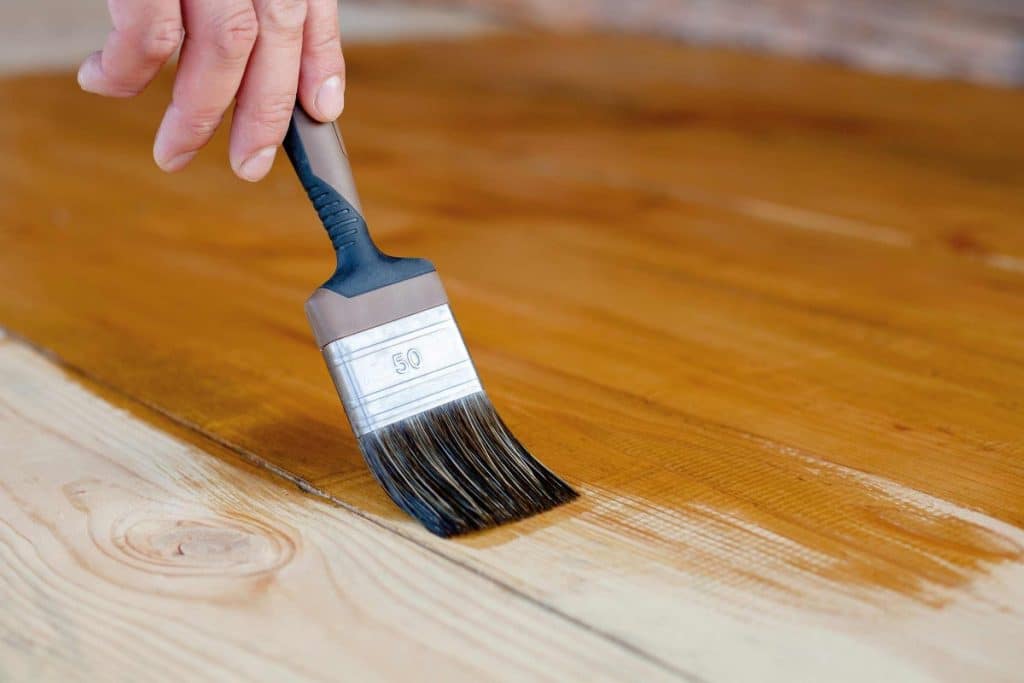 homme entrain d'appliquer de la teinture à du bois décapé